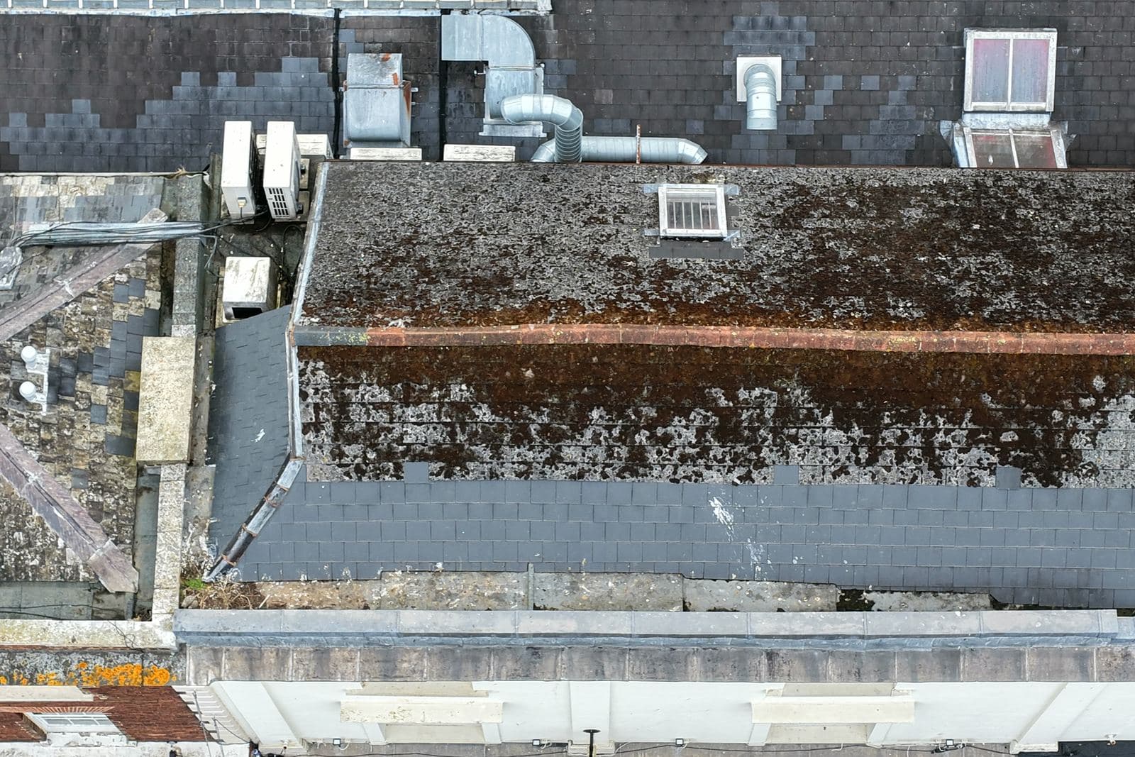 Overhead aerial view of a box gutter running between two roof slopes with a heavy build up of moss and organic debris along the channel