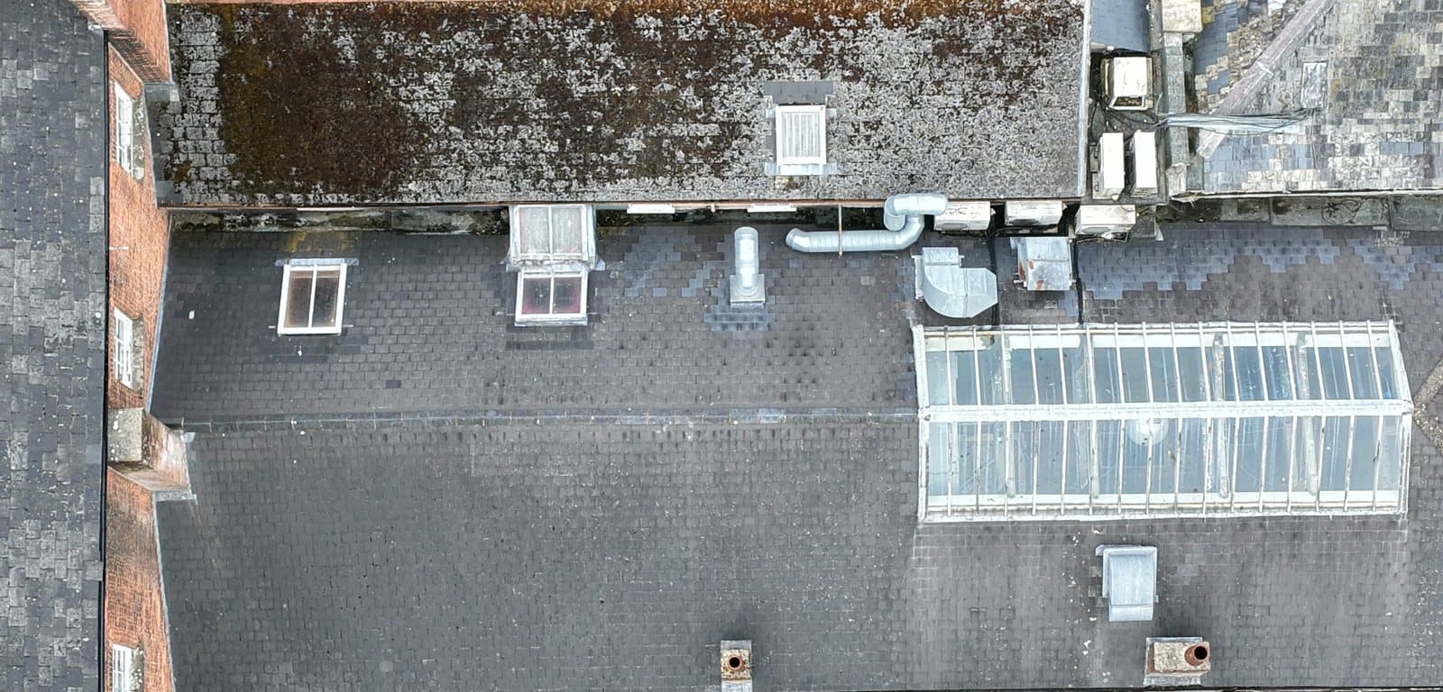 Overhead aerial view of a city centre commercial roof showing a long glazed lantern light, roof mounted air conditioning plant and ductwork, rooflights and parapets