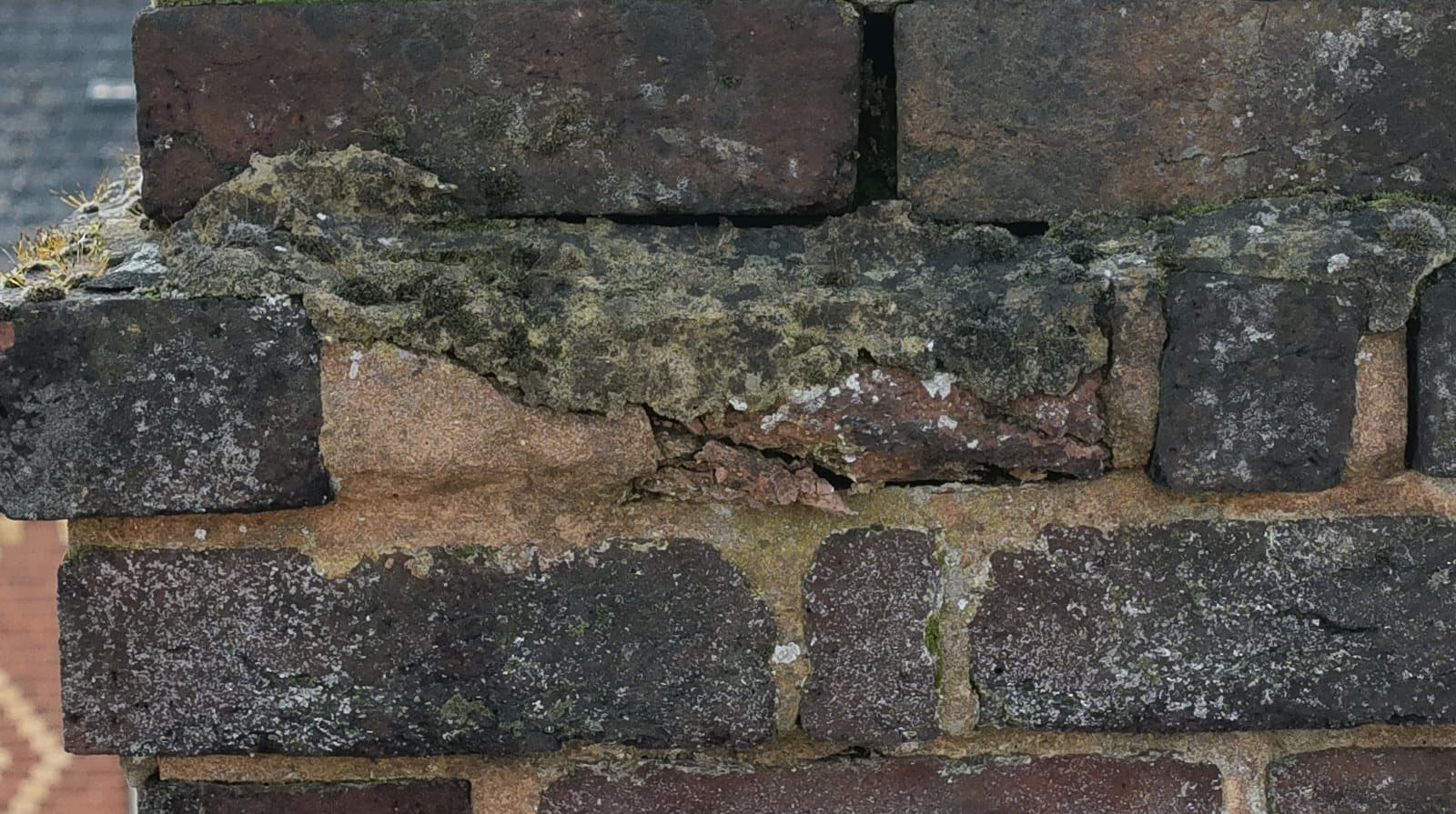 Close aerial view of Victorian chimney brickwork with severely eroded and receded mortar joints and a spalled brick course