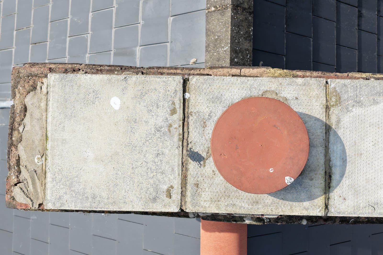 Overhead aerial view of the head of a Victorian chimney stack showing a concrete slab cap and eroded brickwork at the edge, surrounded by natural slate