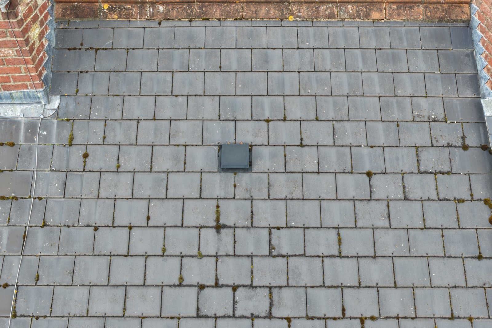 Close aerial view of a natural slate roof slope with a ridge running across the top and moss growing in the joints between slates