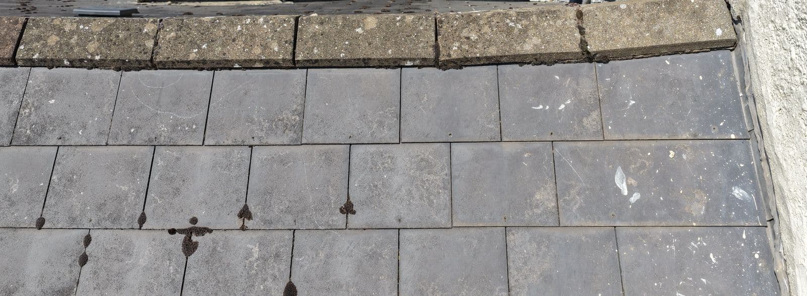 Aerial close up of ridge tiles along a slate roof with open gaps where the bedding mortar has been lost