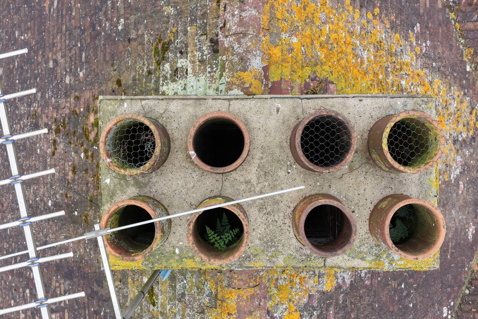 Overhead aerial view of a chimney stack head with eight terracotta pots in a four by two grid, some covered with loose degraded chicken wire and the rest completely open