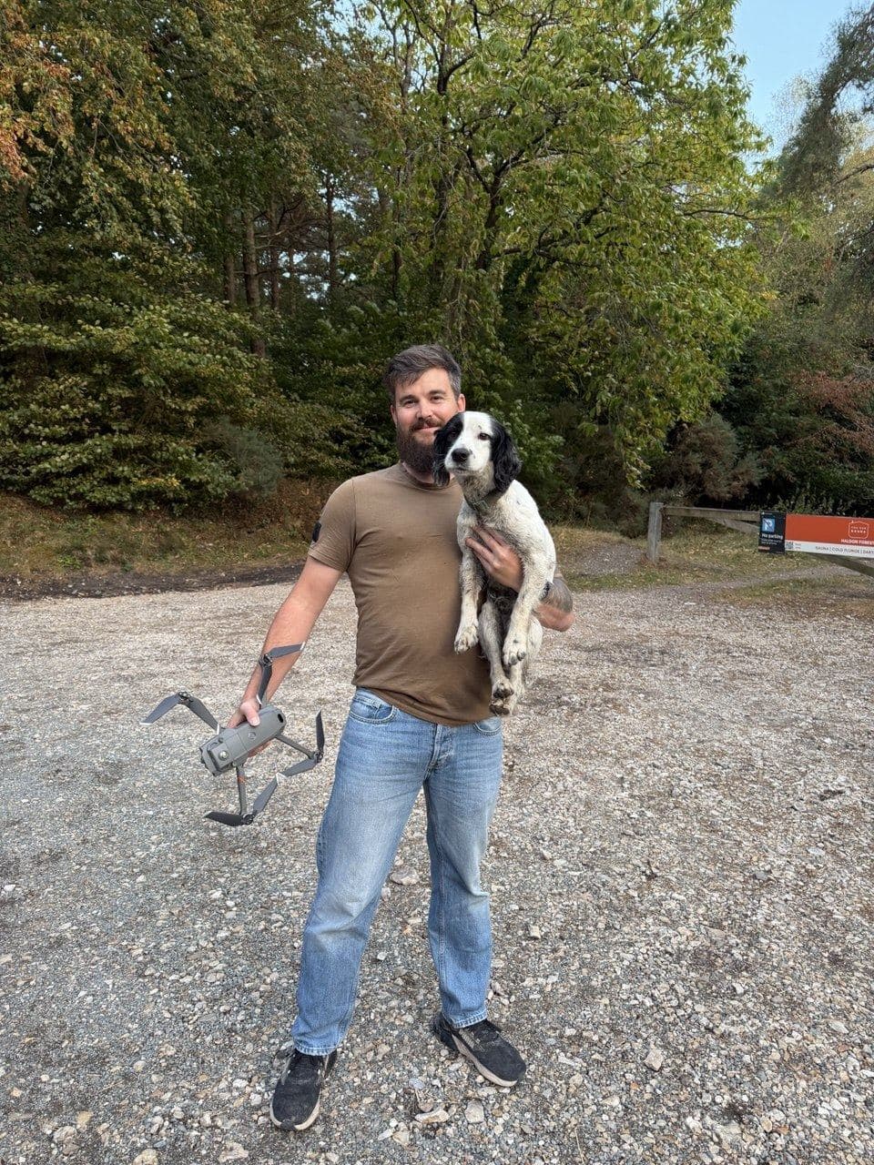 Exeter Drone Surveys operator holding the found black and white spaniel in the Haldon Forest car park, with the folded drone in his other hand