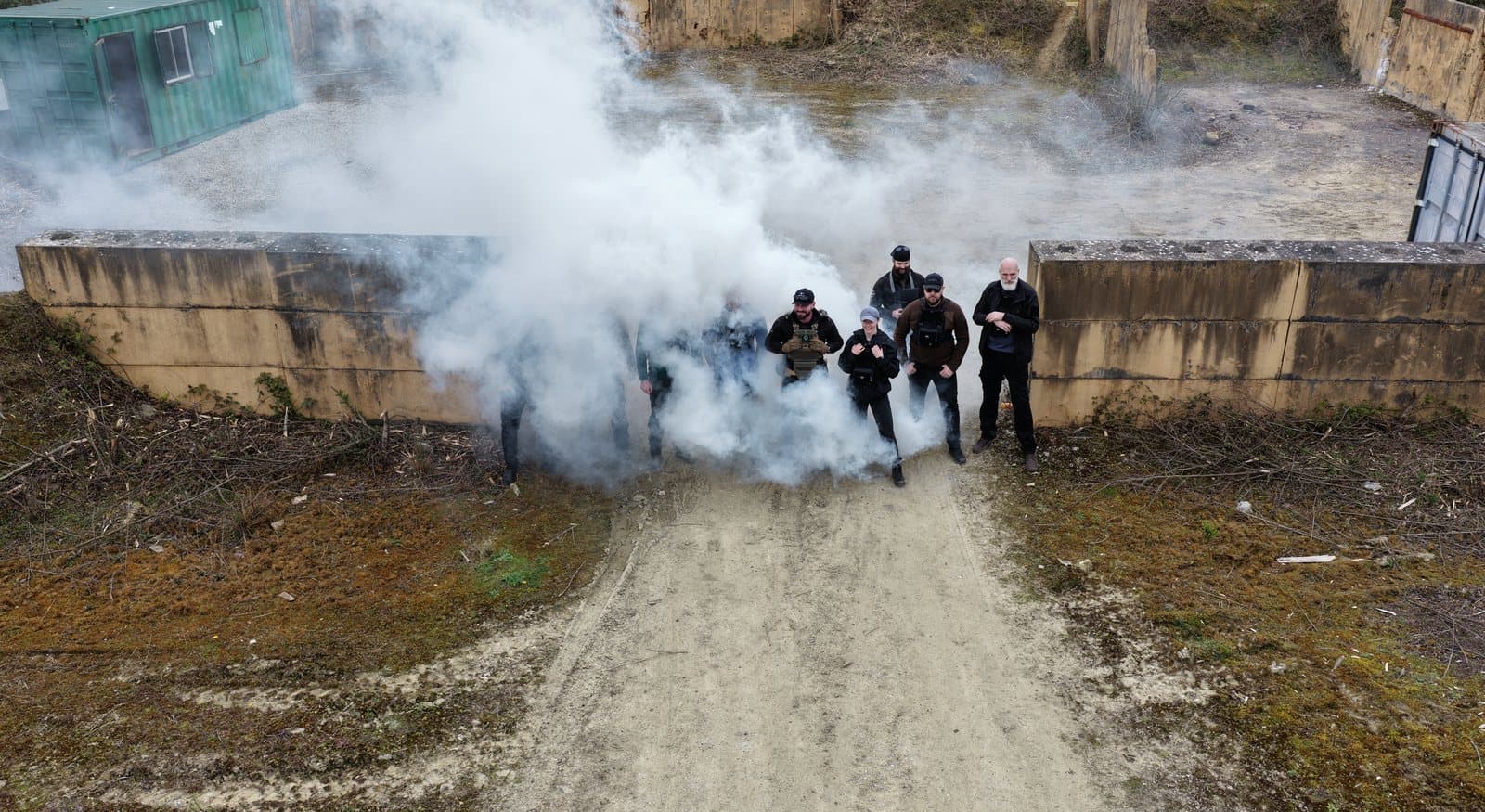 Aerial view of white smoke drifting across a training compound and partially obscuring the course group formed up below